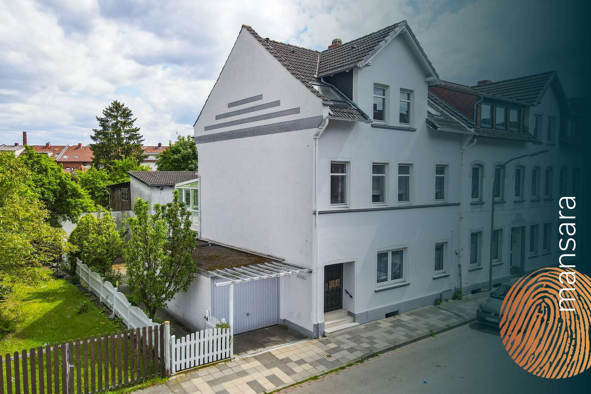 Moderne Wohngebäude mit einem Garten und einer gepflasterten Einfahrt, umgeben von Bäumen und Sträuchern.