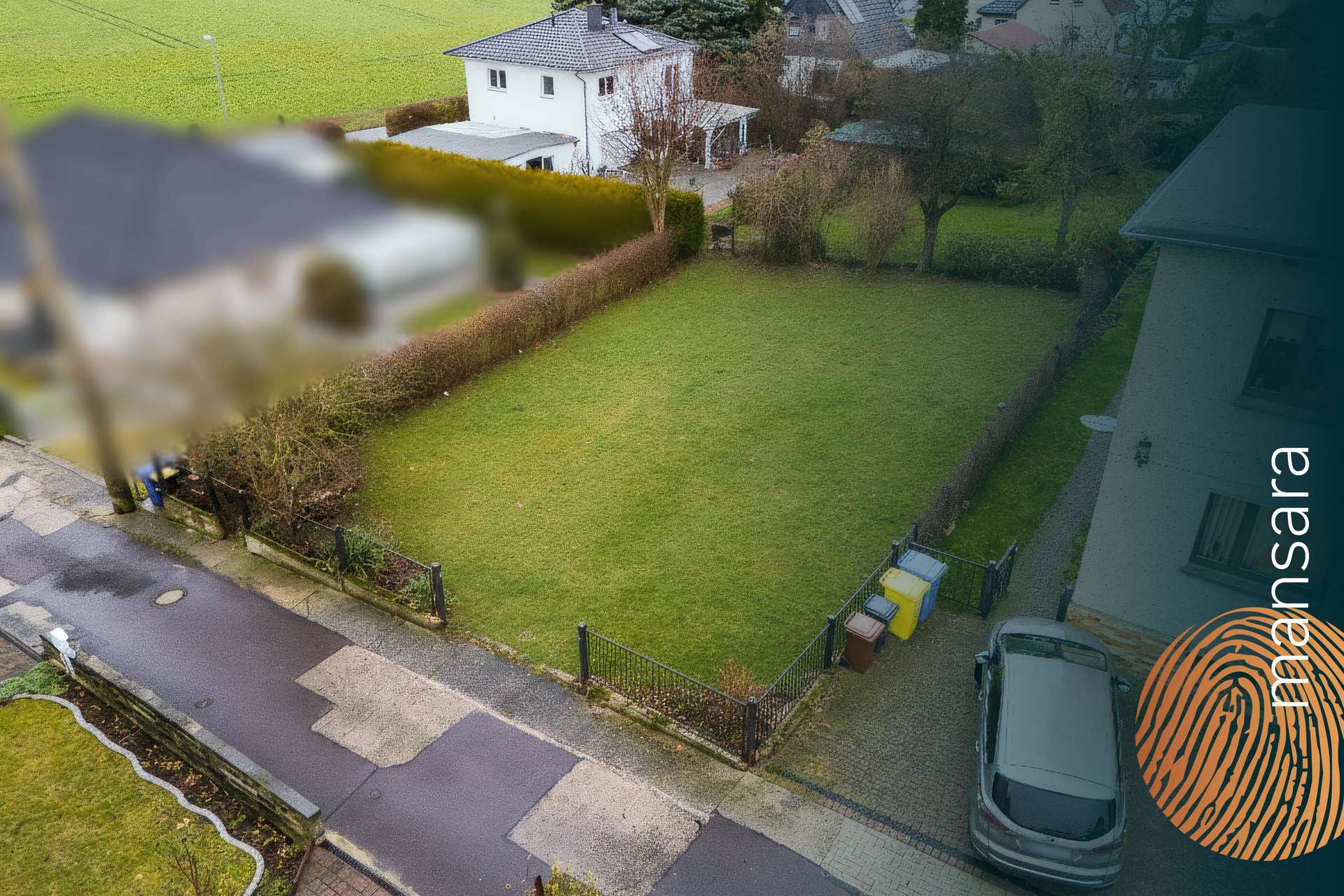 Luftaufnahme eines gepflegten Rasens umgeben von Hecken, mit Wohnhäusern und einer ruhigen Straße im Hintergrund.