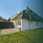 Ein modernes Haus mit einem Satteldach, Gartenmöbeln im Freien und einer gepflegten Rasenfläche.