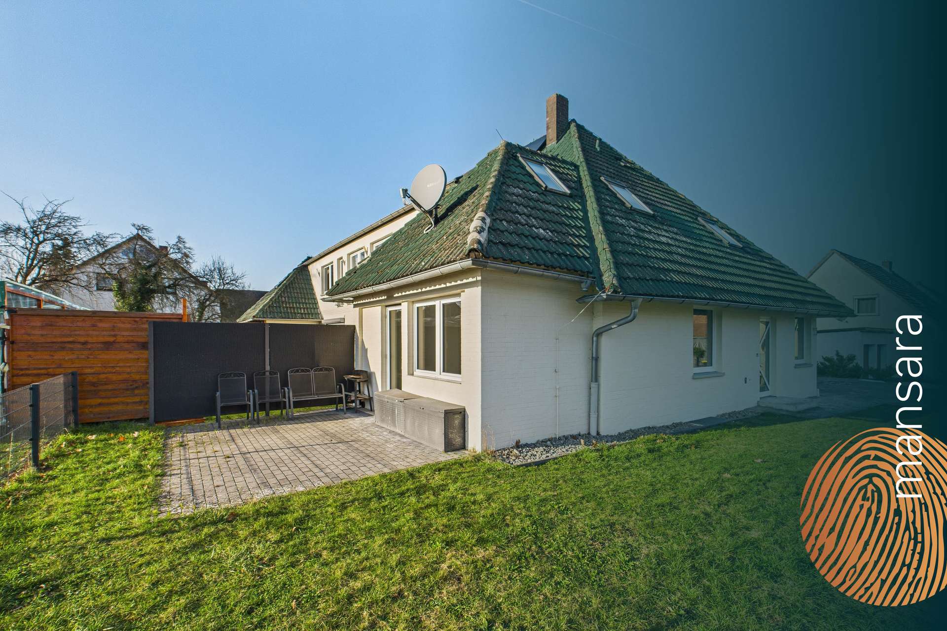 Ein modernes Haus mit einem Satteldach, Gartenmöbeln im Freien und einer gepflegten Rasenfläche.