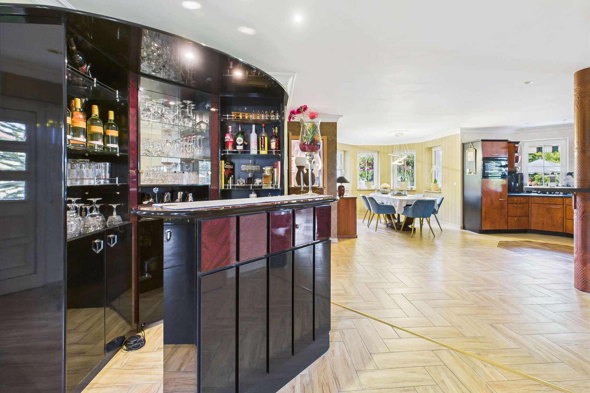 Elegante Hausbar mit Glasregalen und Holzdetails, umgeben von einem offenen Wohnbereich und modernen Möbeln.