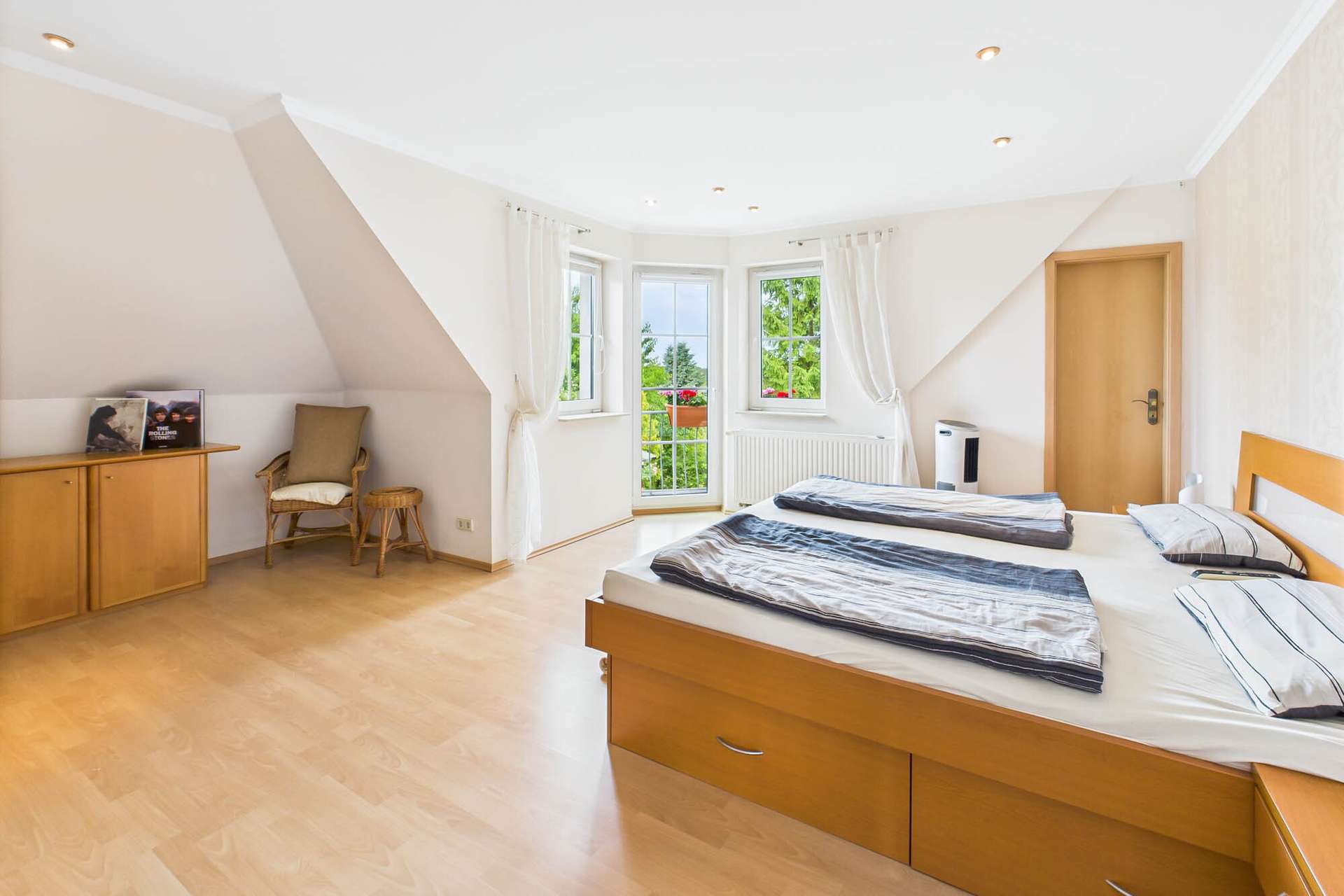 Helles Schlafzimmer mit Doppelbett, Holzschränken und Fenstern mit Blick ins Grüne.