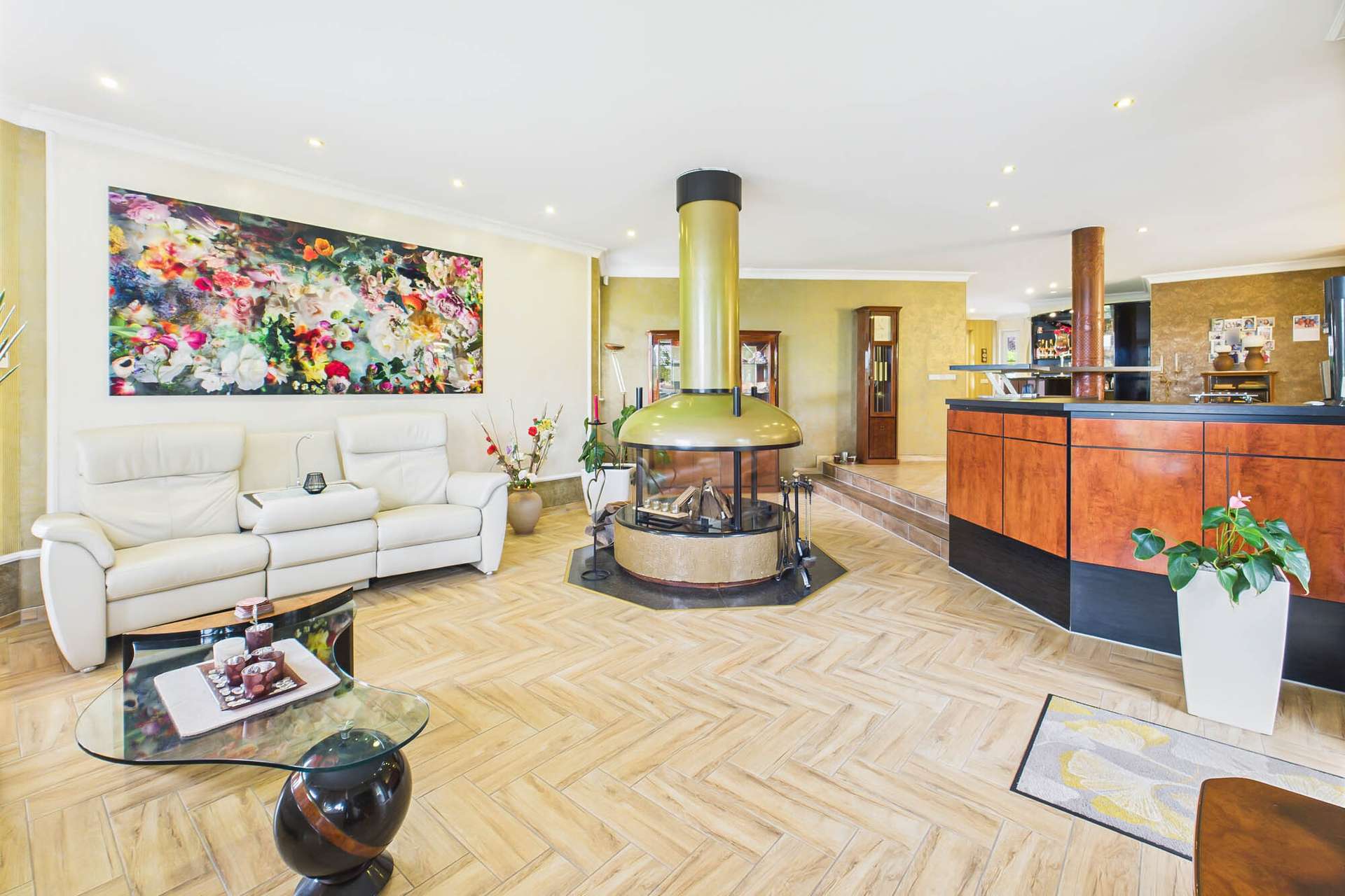 Moderne Wohnzimmer mit einem zentralen Kamin, eleganter Couch, Glas-Tisch und buntem Wandbild.