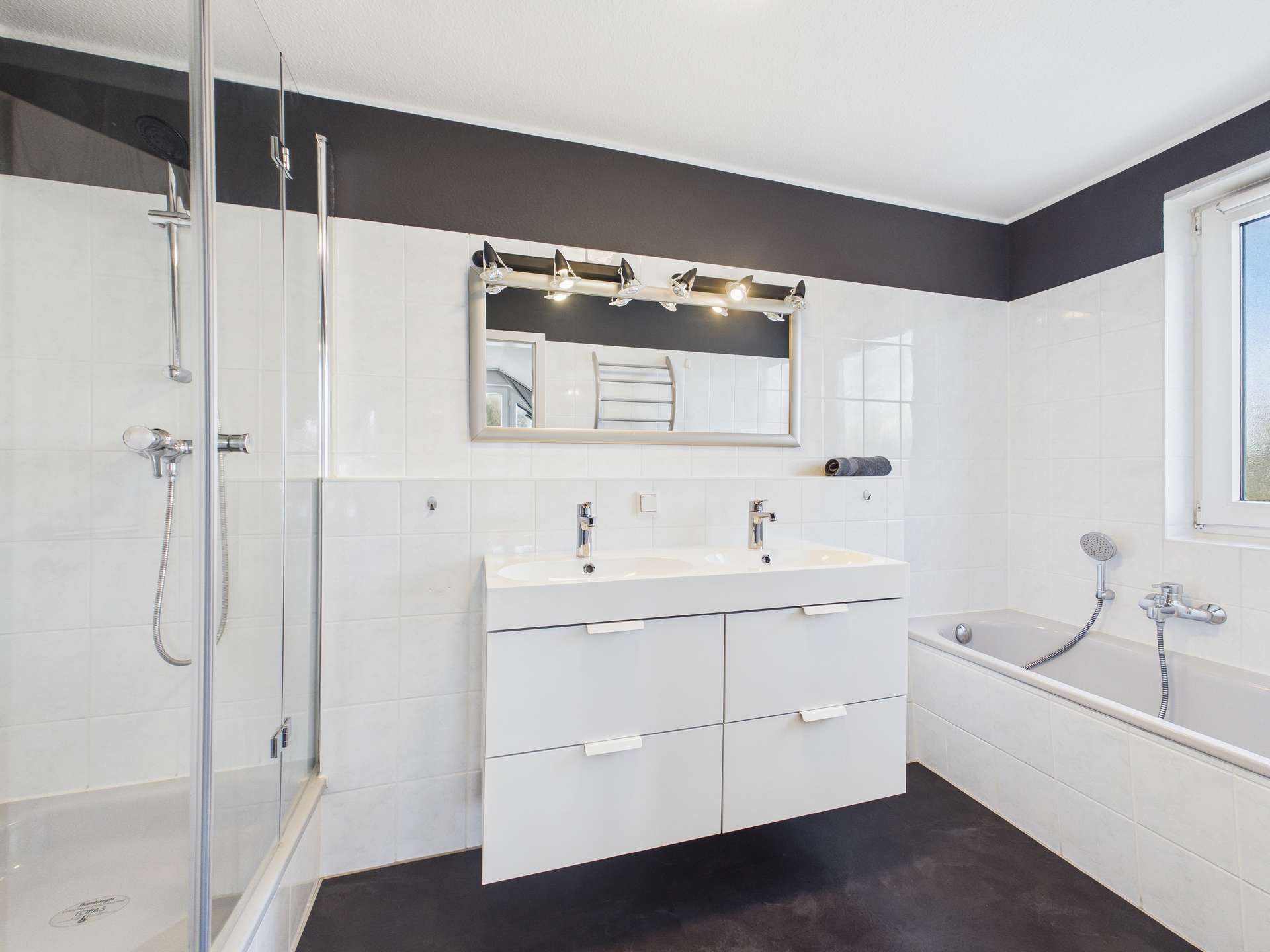 Modernes Badezimmer mit Dusche, Badewanne und Doppelwaschtisch vor einem schwarzen Akzentwand.