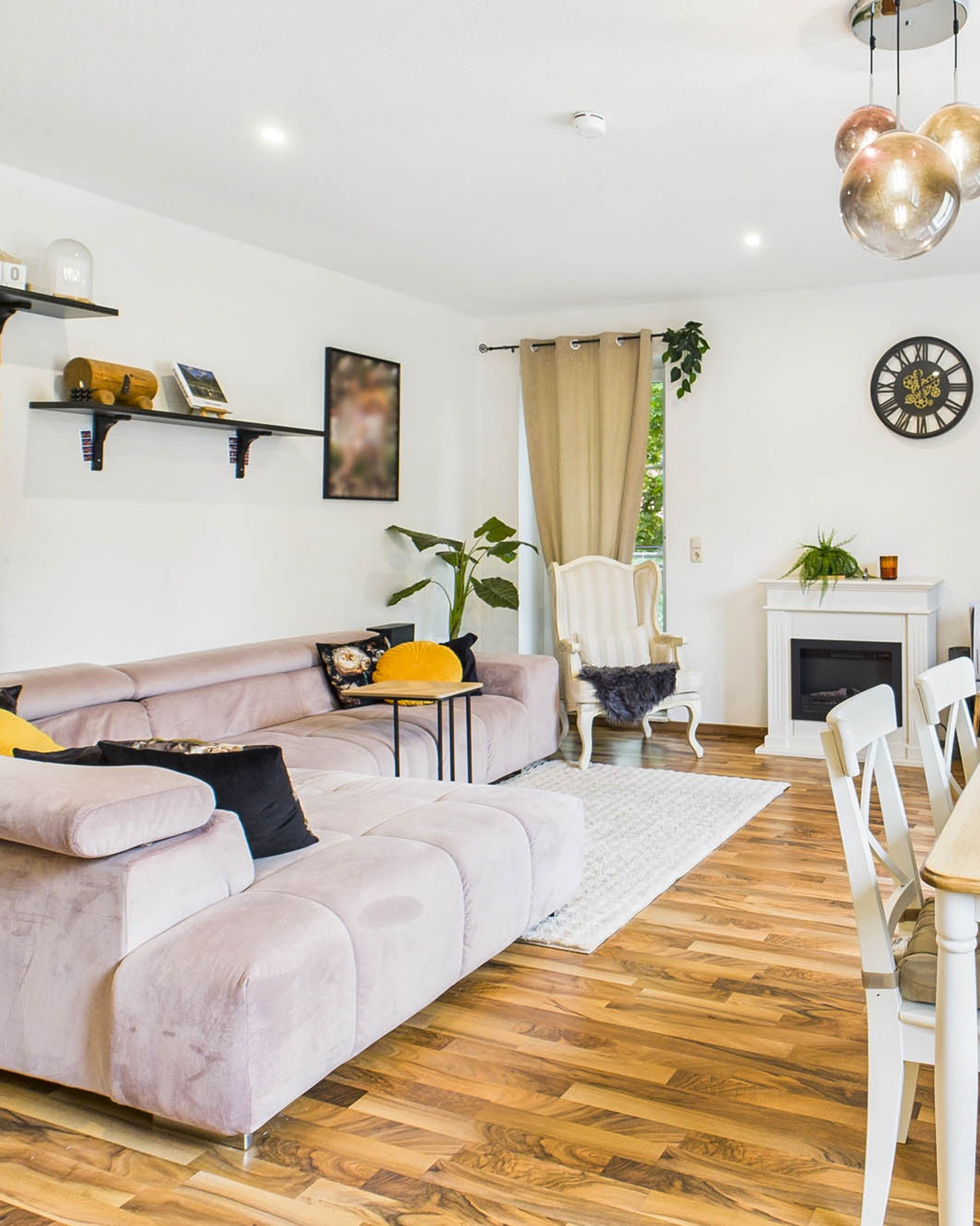 Heller Wohnraum mit beigem Sofa, Holzboden, Pflanzen, Wandregalen und moderner Beleuchtung.