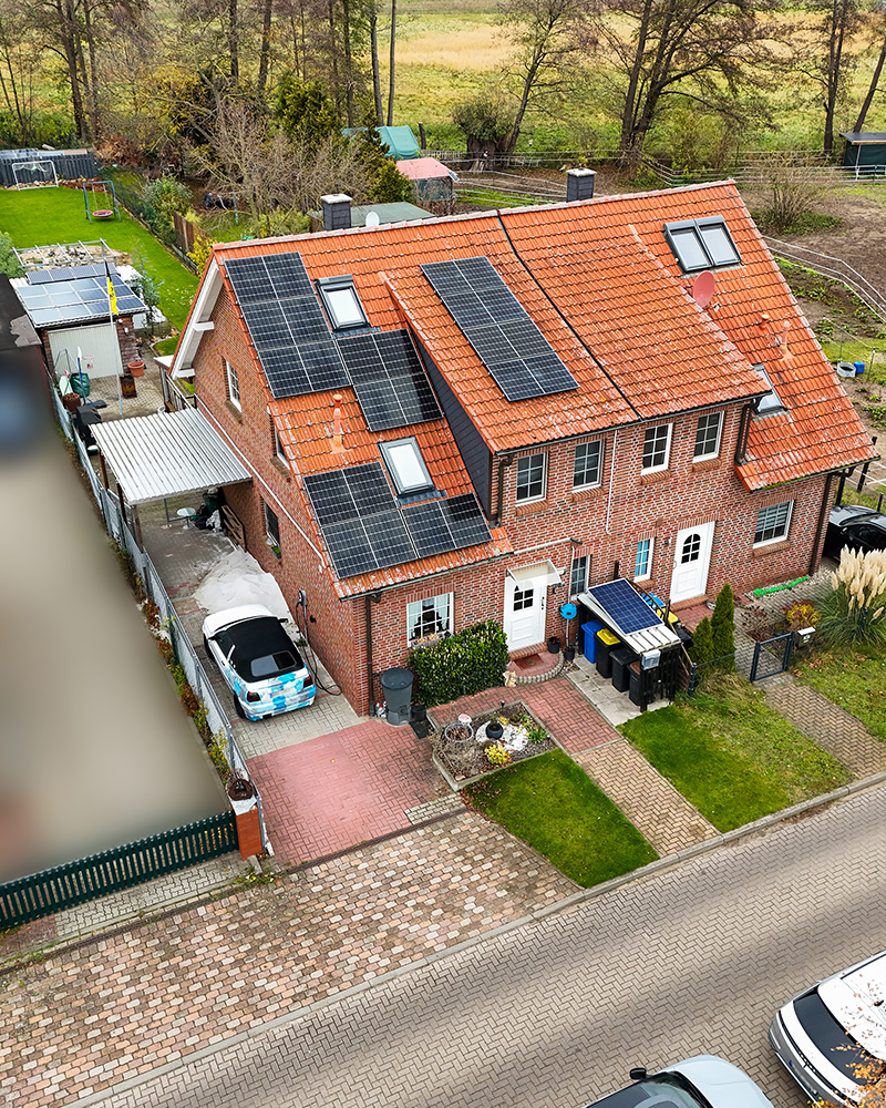 Zweifamilienhaus mit roten Ziegeldach, Solarpanelen und angrenzendem Garten, umgeben von gepflegten Wegen und ParkplÀtzen.