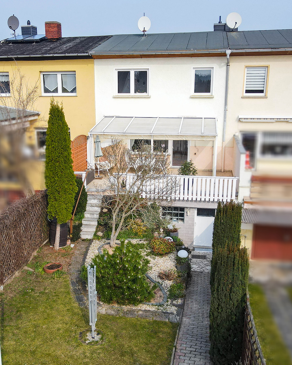 Hintergarten mit Terrasse, Rasen, BÀumen und Gartenweg zwischen zwei WohnhÀusern.