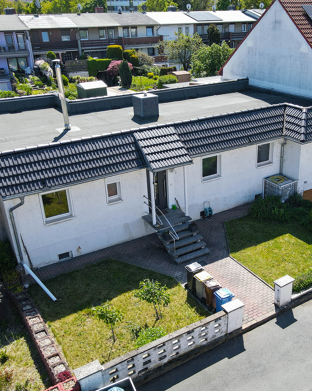 Ein modernes Einfamilienhaus mit Garten, gepflastertem Weg und MĂŒlltonnen im Vordergrund.