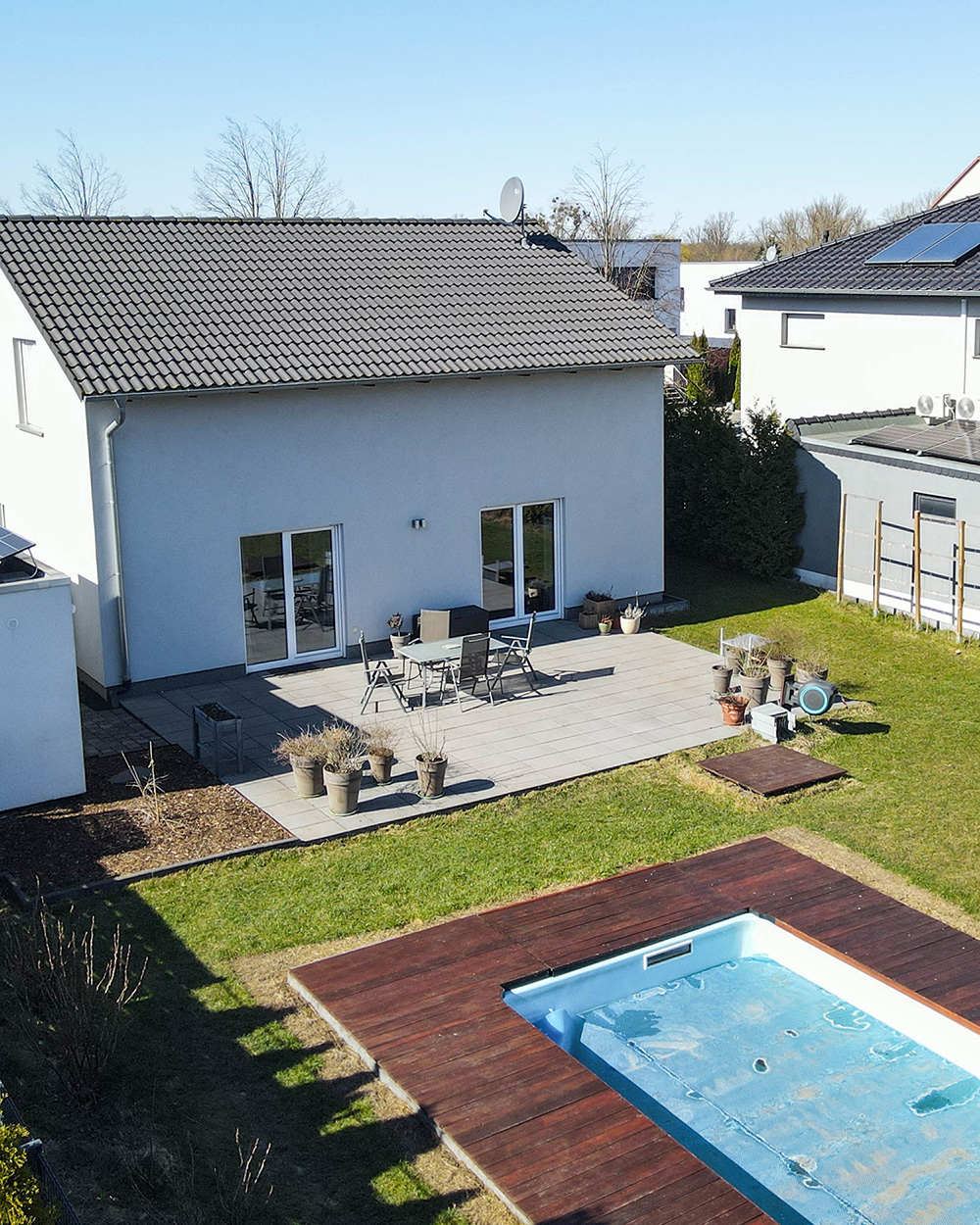 Moderne Villa mit Terrasse, Garten und leerem Pool, umgeben von weiteren Wohnhäusern.
