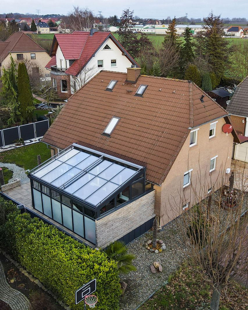 Ein Einfamilienhaus mit einem modernen Wintergarten, umgeben von gepflegten GĂ€rten und einer ruhigen Nachbarschaft.