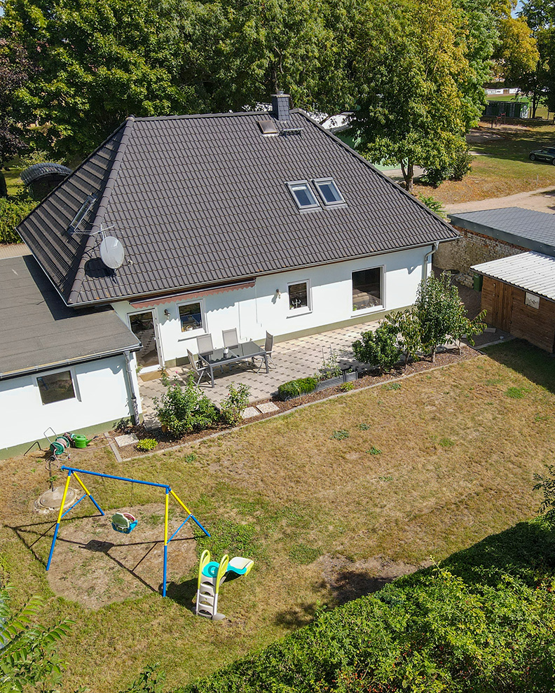 Ein Einfamilienhaus mit einem Garten, Schaukel und Terrasse, umgeben von BĂ€umen und angrenzenden Garagen.