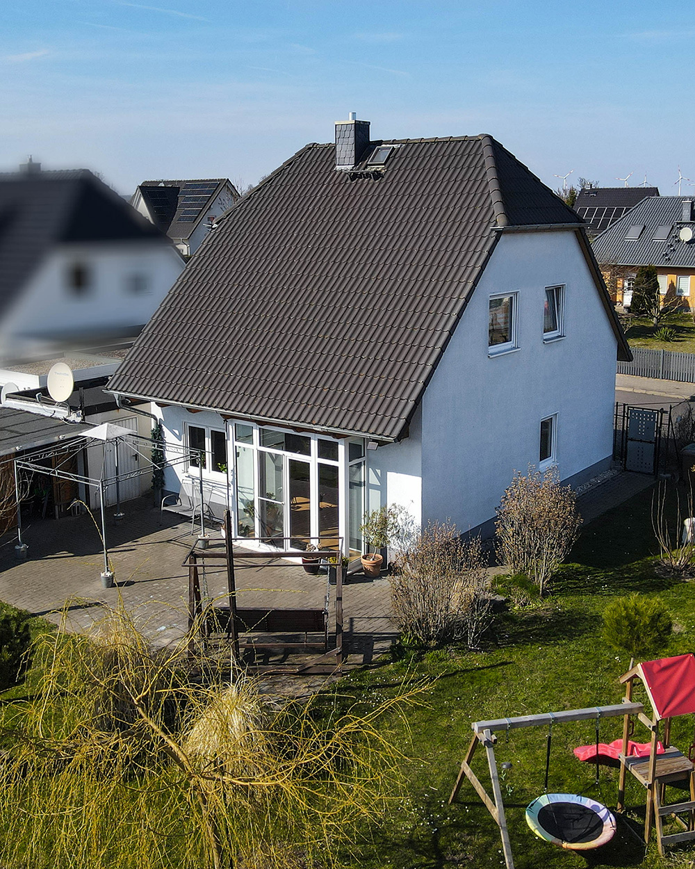 Ein zweigeschossiges Einfamilienhaus mit Satteldach, umgeben von Garten und Spielplatz, unter blauem Himmel.