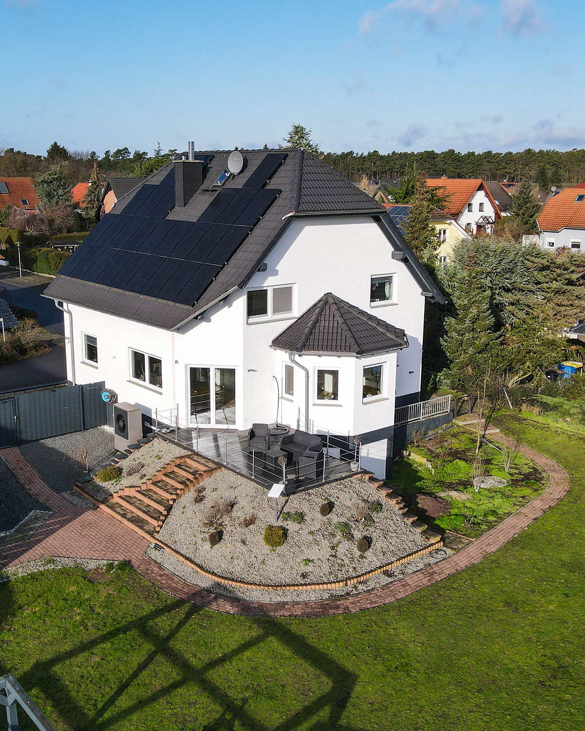 Modernes Einfamilienhaus mit Solarpanelen, Garten und Terrasse in einer ruhigen Wohngegend.