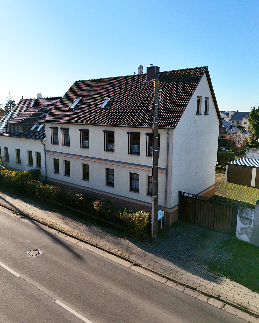 Zweigeschossiges Wohnhaus mit Satteldach, Fenster mit RolllĂ€den und angrenzendem Garten an einer ruhigen StraĂe.