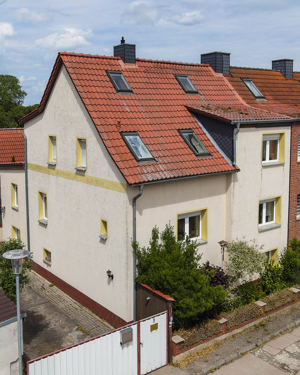Zweistöckiges Wohnhaus mit rotem Satteldach, Dachfenstern und umgebendem Garten in einer ruhigen Wohngegend.