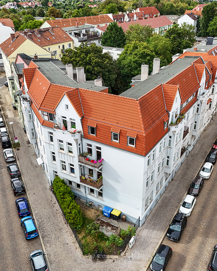 Eine moderne Wohnanlage mit rotem Satteldach und Balkonen, umgeben von BĂ€umen und parkenden Autos.