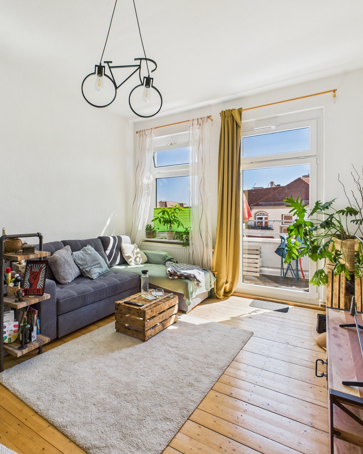 Heller Wohnraum mit grauem Sofa, Holztisch, Pflanzen und groĂen Fenstern, die auf einen Balkon blicken.