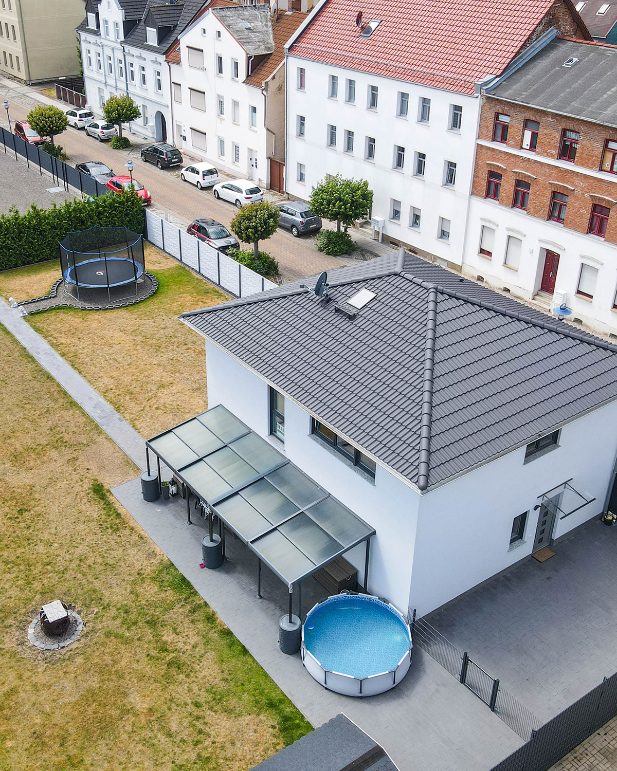 Luftaufnahme eines modernen Hauses mit Garten, Pool und umliegenden WohngebÀuden in einer ruhigen Nachbarschaft.