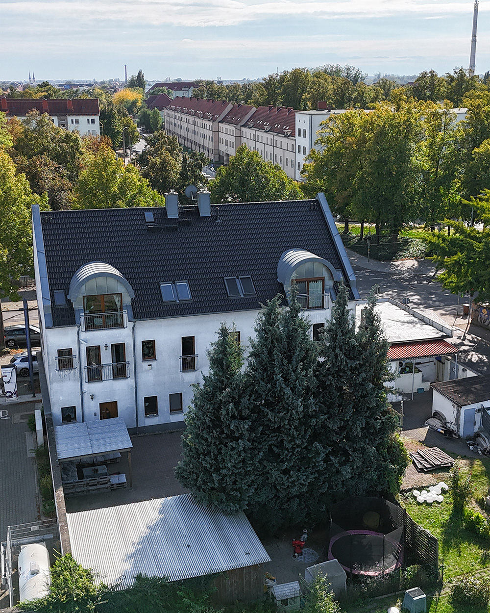Blick auf ein mehrstöckiges Wohnhaus mit begrĂŒntem Innenhof und umliegenden BĂ€umen in einer stĂ€dtischen Umgebung.