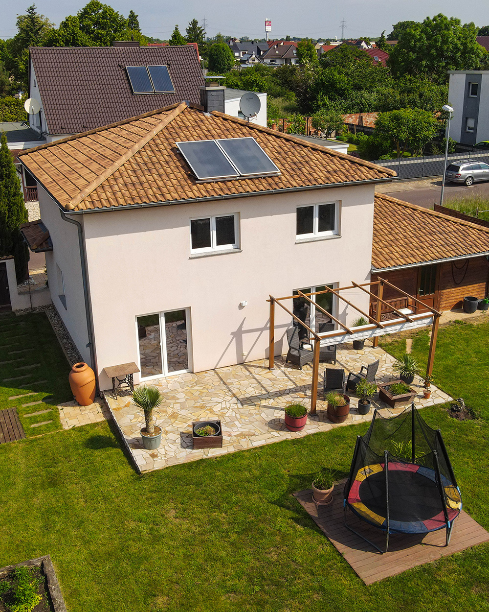 Ein modernes Einfamilienhaus mit Solarzellen, Terrasse und Garten, umgeben von Rasen und Pflanzen.