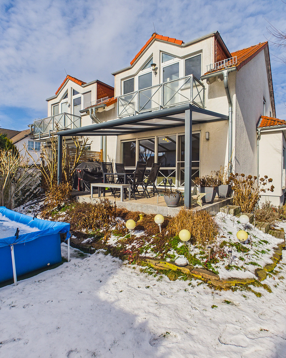 Moderne DoppelhaushÀlfte mit Balkon, Gartenmöbeln und schneebedecktem Boden, umgeben von einem gepflegten Garten.