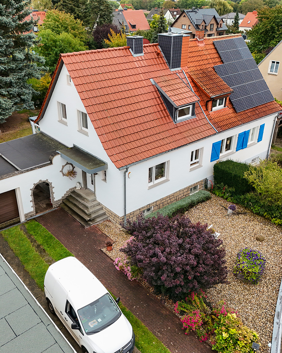 Ein Einfamilienhaus mit rotem Dach, Solarpanelen und gepflegtem Garten, umgeben von weiteren WohnhÀusern.