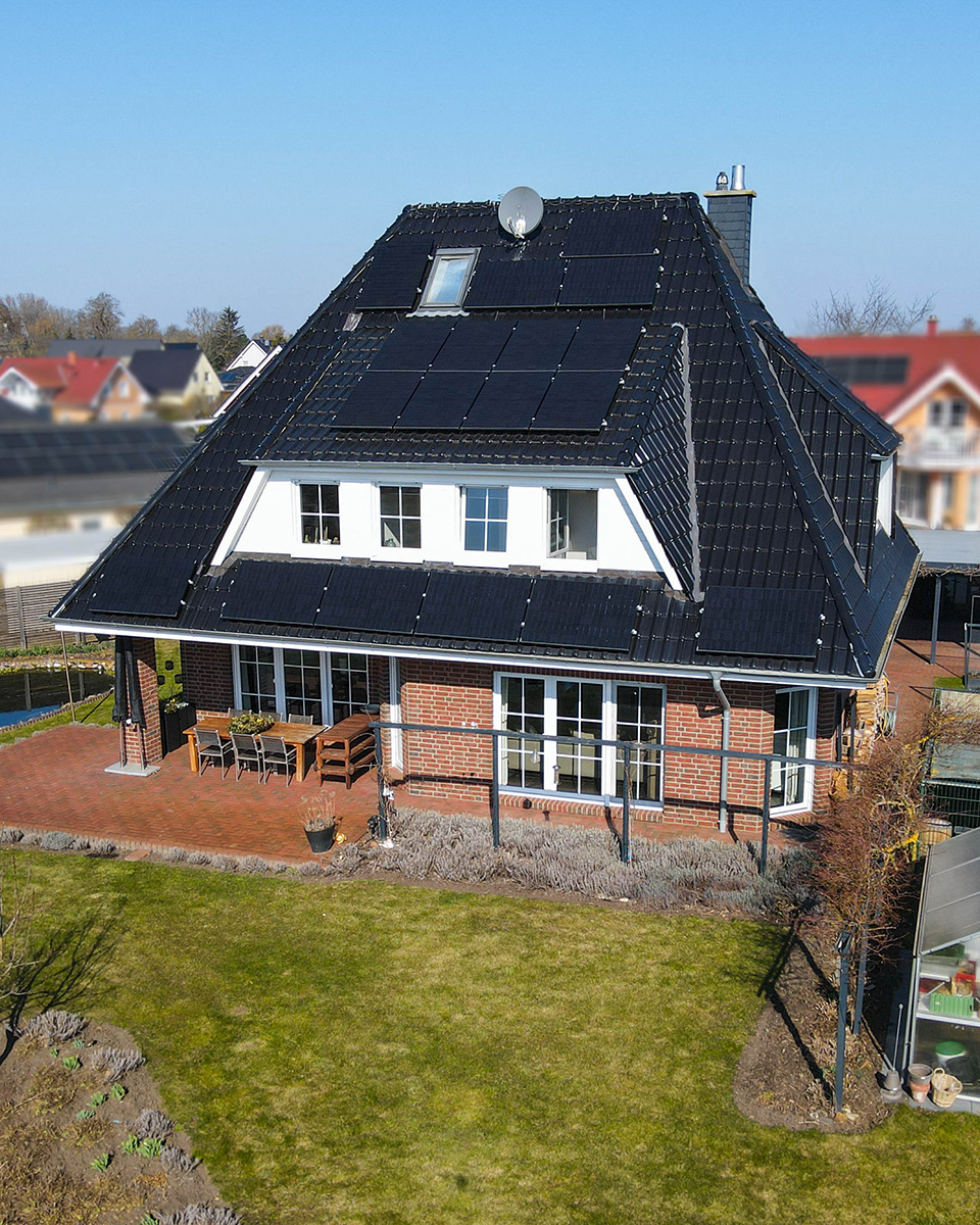 Ein modernes Einfamilienhaus mit schwarzer Dachdeckung und Solarpanelen, umgeben von einem gepflegten Garten.
