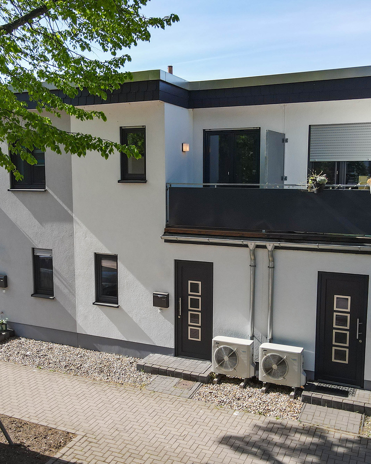 Moderne Wohngebäude mit weißer Fassade, Balkon und zwei Klimaanlagen im Erdgeschoss.