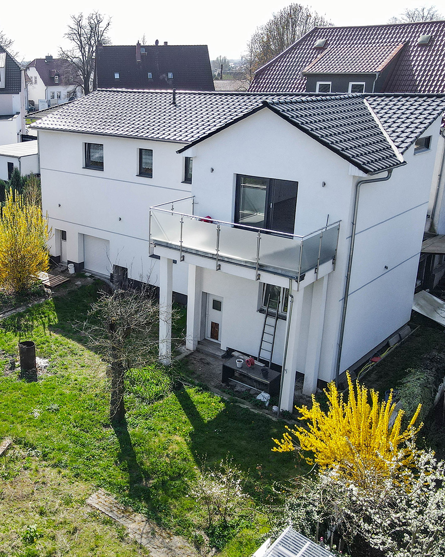 Modernes, zweigeschossiges Wohnhaus mit Balkon, umgeben von einem grĂŒnen Garten und StrĂ€uchern.