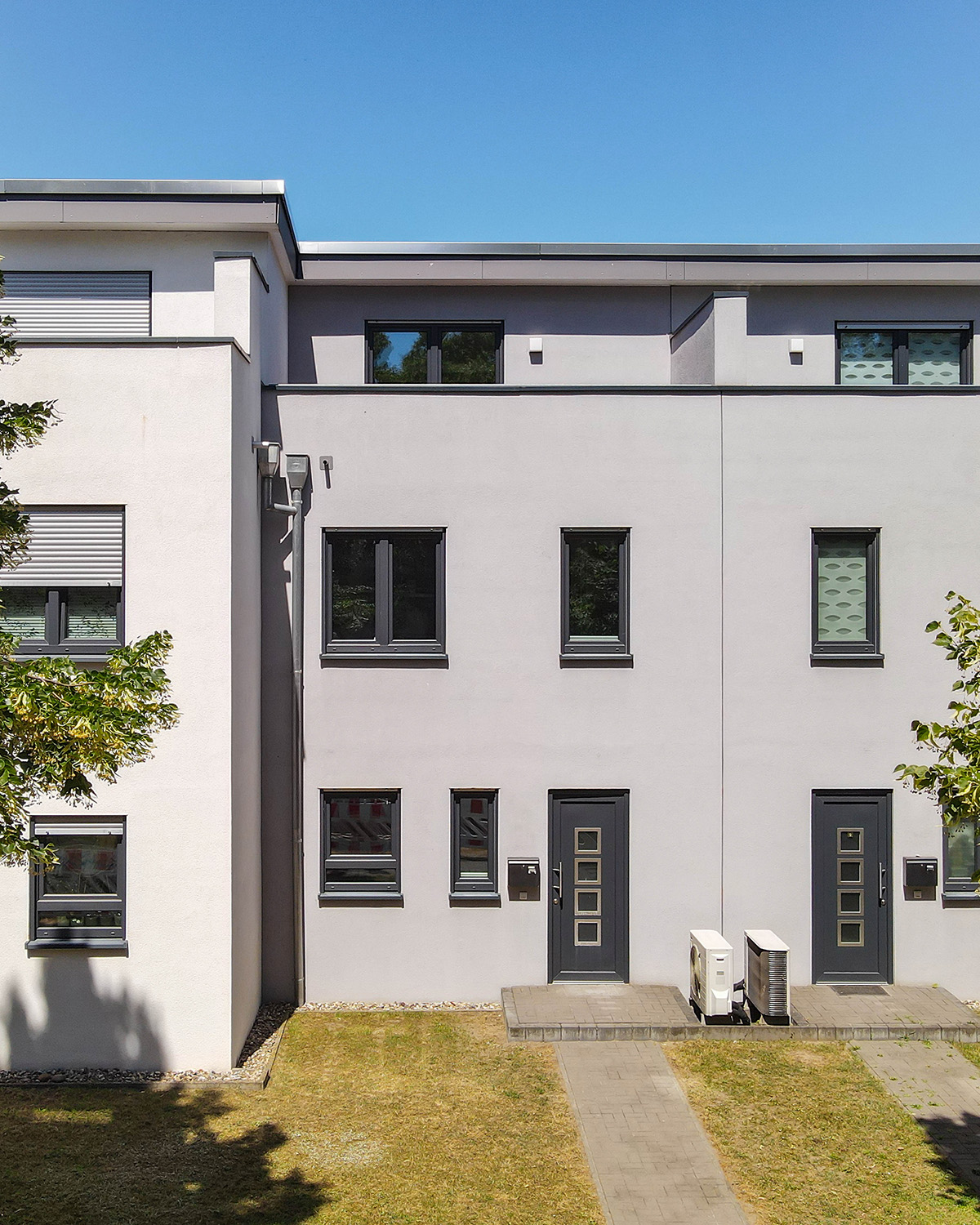 Moderne Wohnhäuser mit grauer Fassade, großen Fenstern und gepflegtem Rasen vor dem Gebäude.