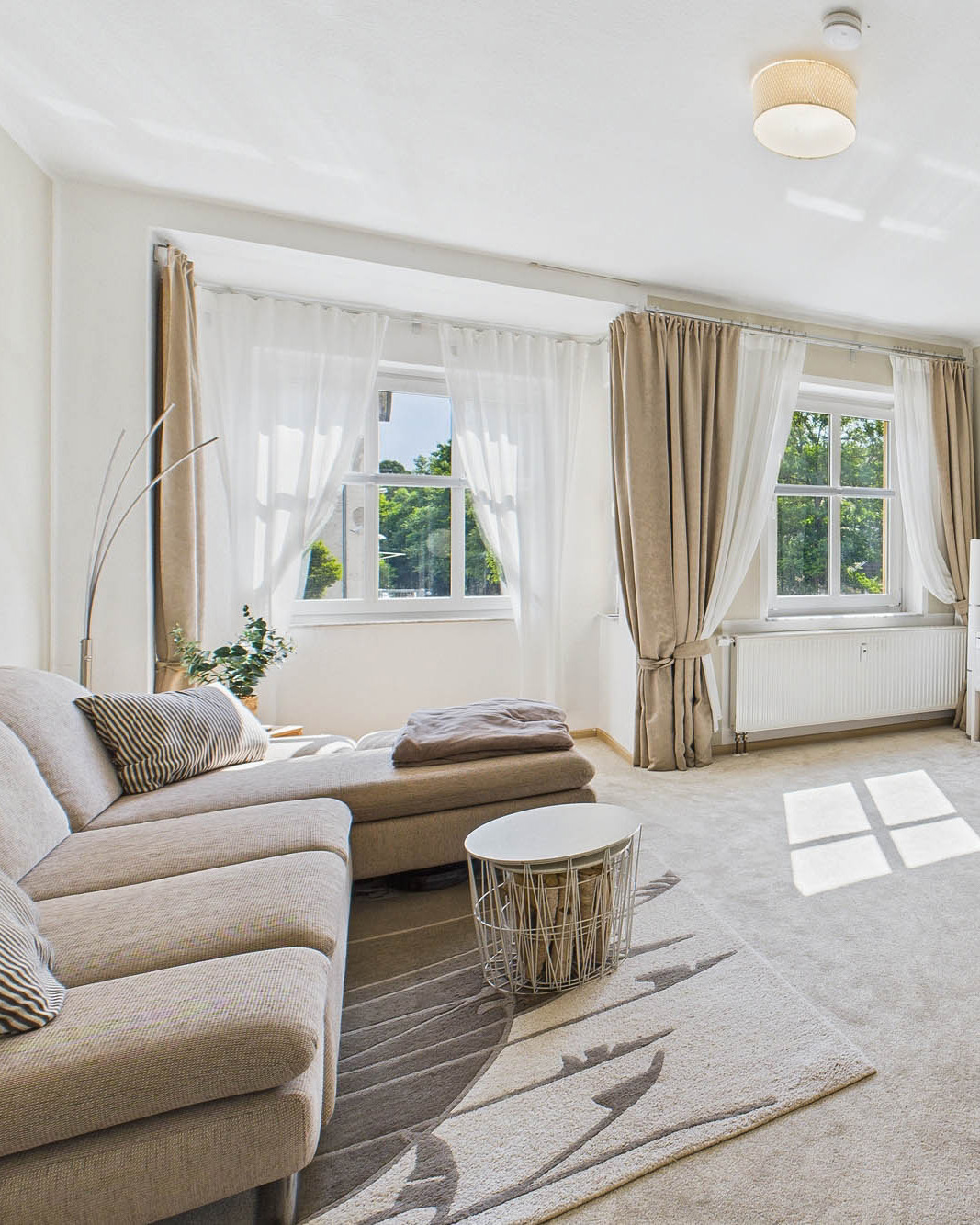 Helles Wohnzimmer mit beigem Sofa, runden Beistelltisch und groĂen Fenstern, die Tageslicht hereinlassen.